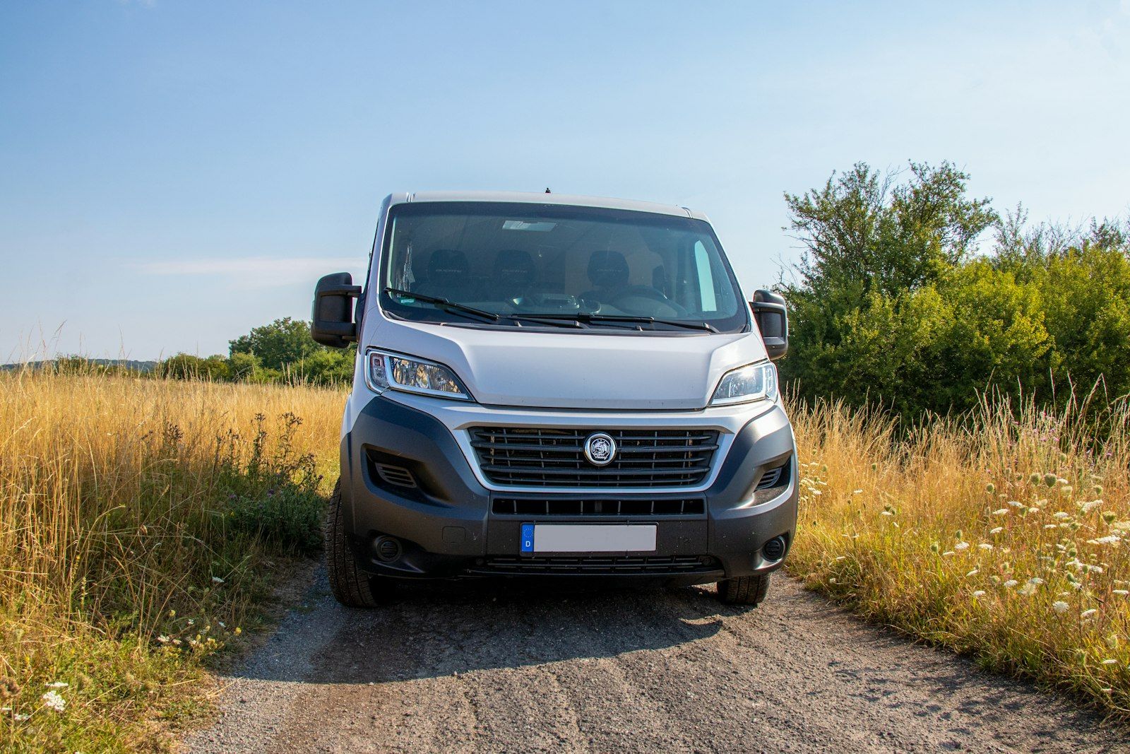Furgoneta Fiat Ducato gris vista de frente en un camino de tierra entre hierba seca.